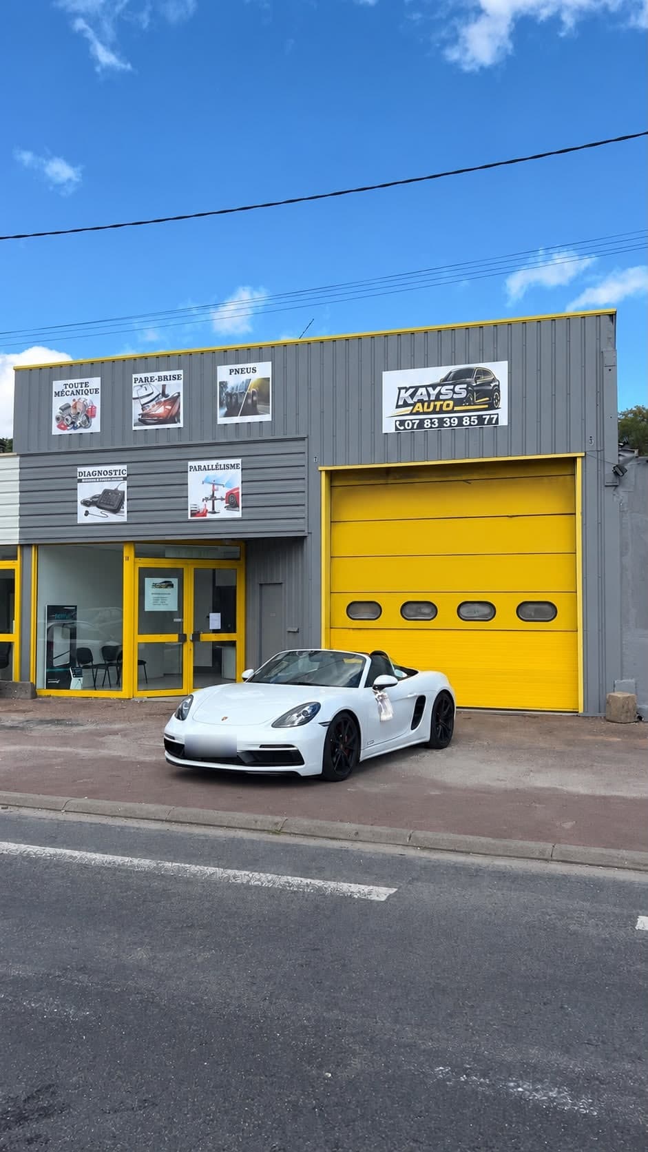 Façade du garage Kayss Auto : bardage gris, grande porte jaune et vitrine d'accueil, une voiture garée devant.